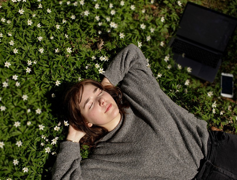 Young,Woman,Laying,In,Green,Grass,Next,To,The,Laptop.