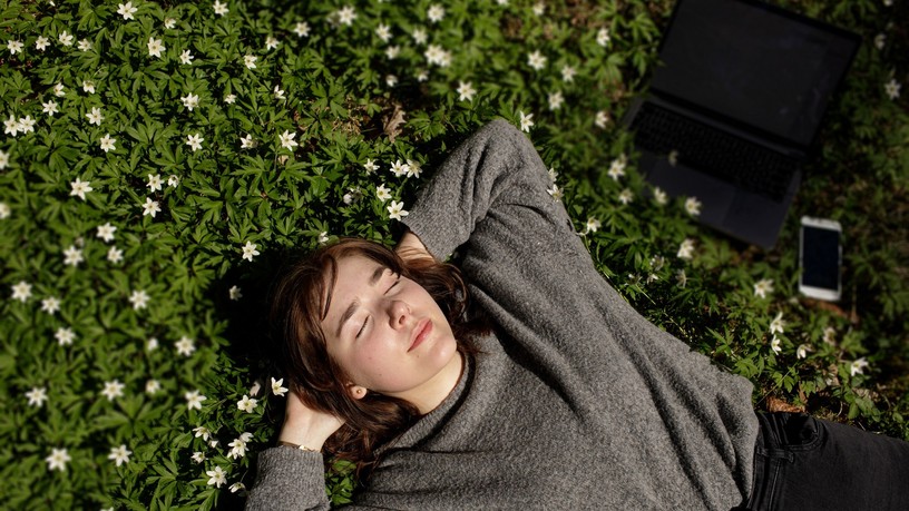 Young,Woman,Laying,In,Green,Grass,Next,To,The,Laptop.